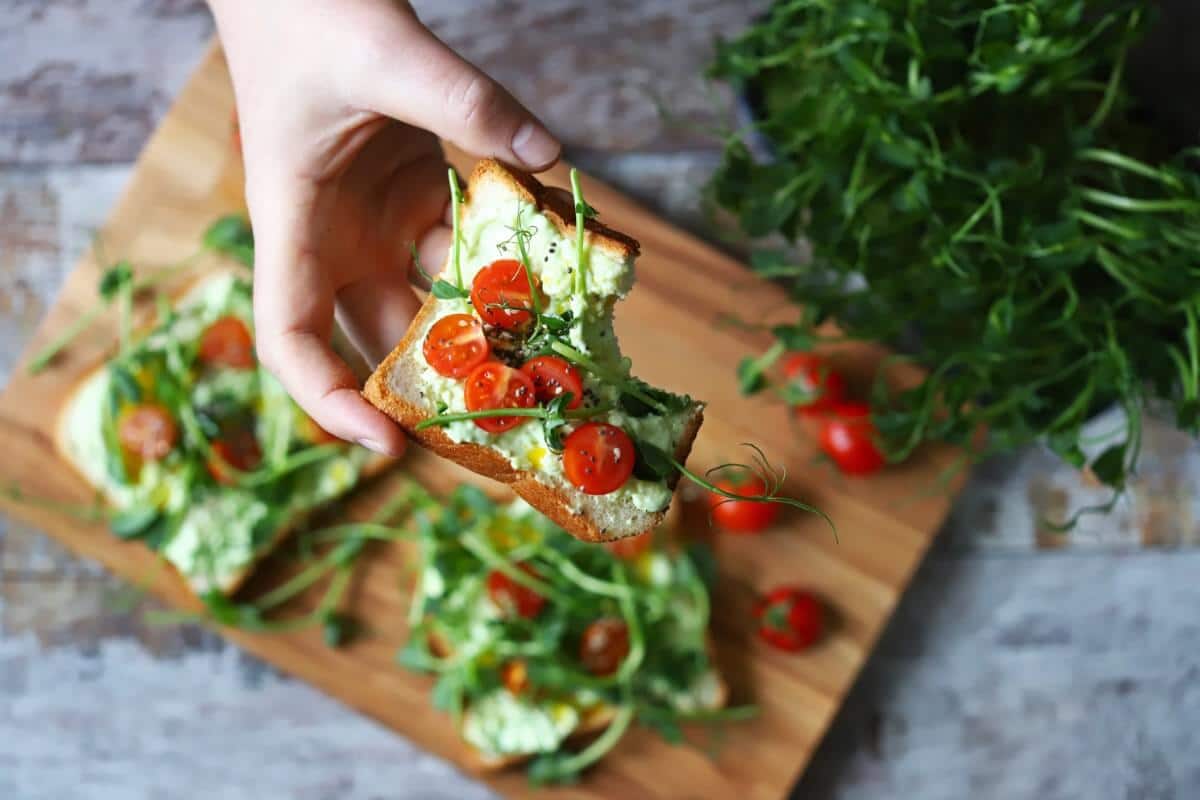 A hand holding a piece of bread with tomatoes and microgreens on it.