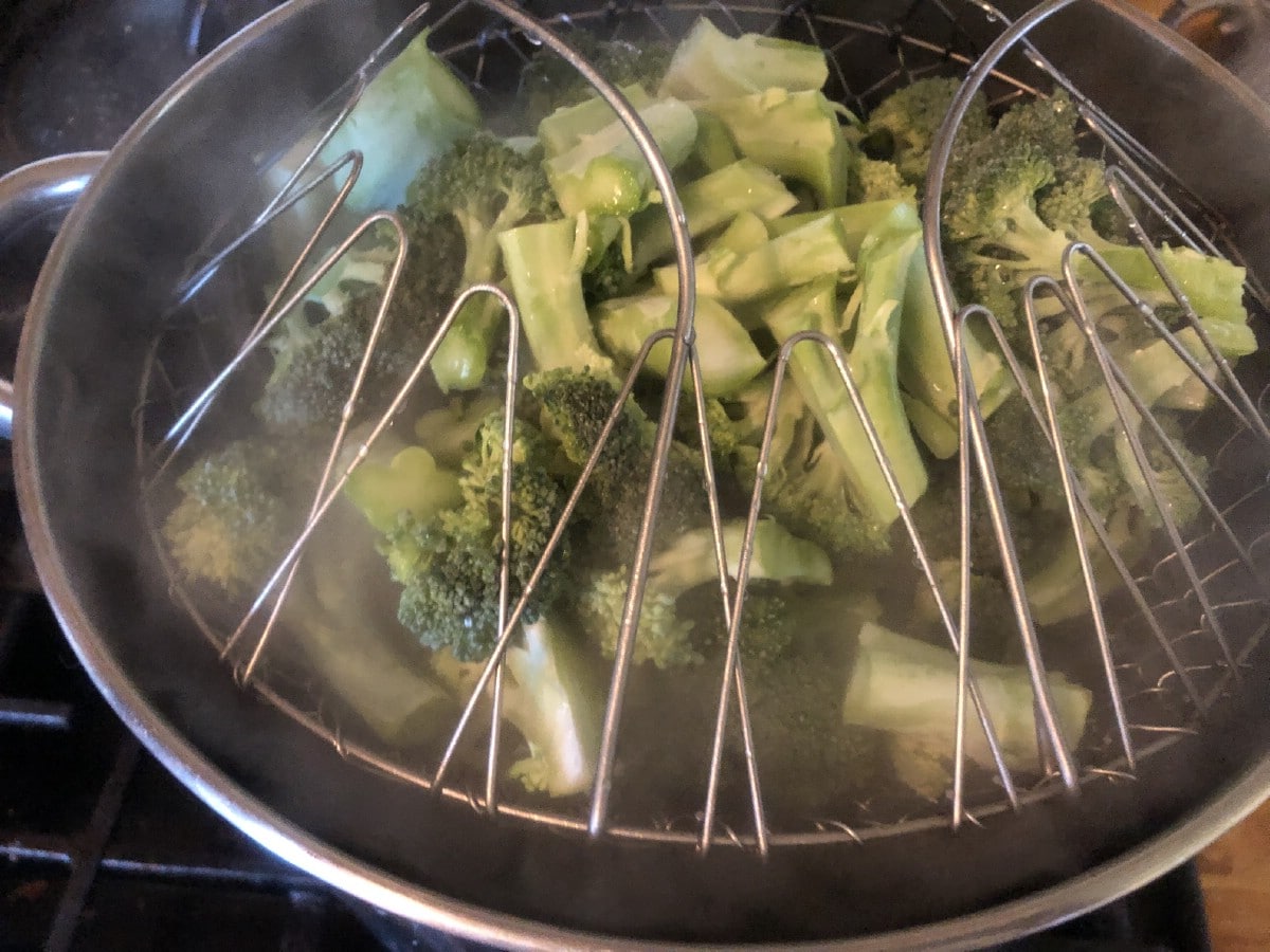folding wire mesh basket filled with broccoli being lowered into blanching water