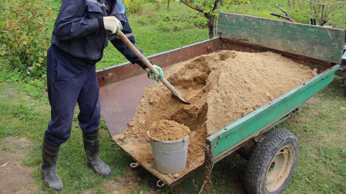 man shoveling sand into bucket for tool storage