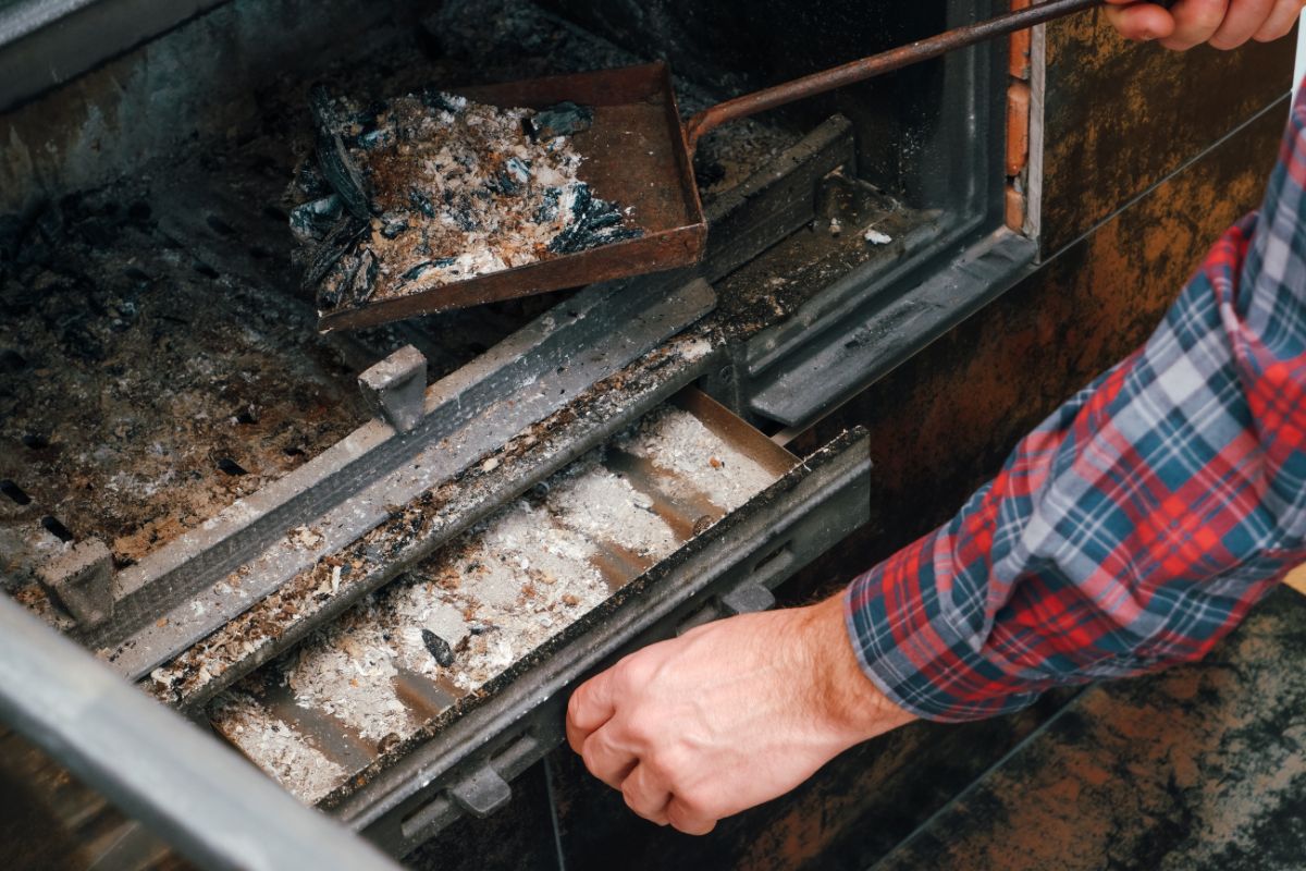 man cleaning out the ash pan on a wood burning stove