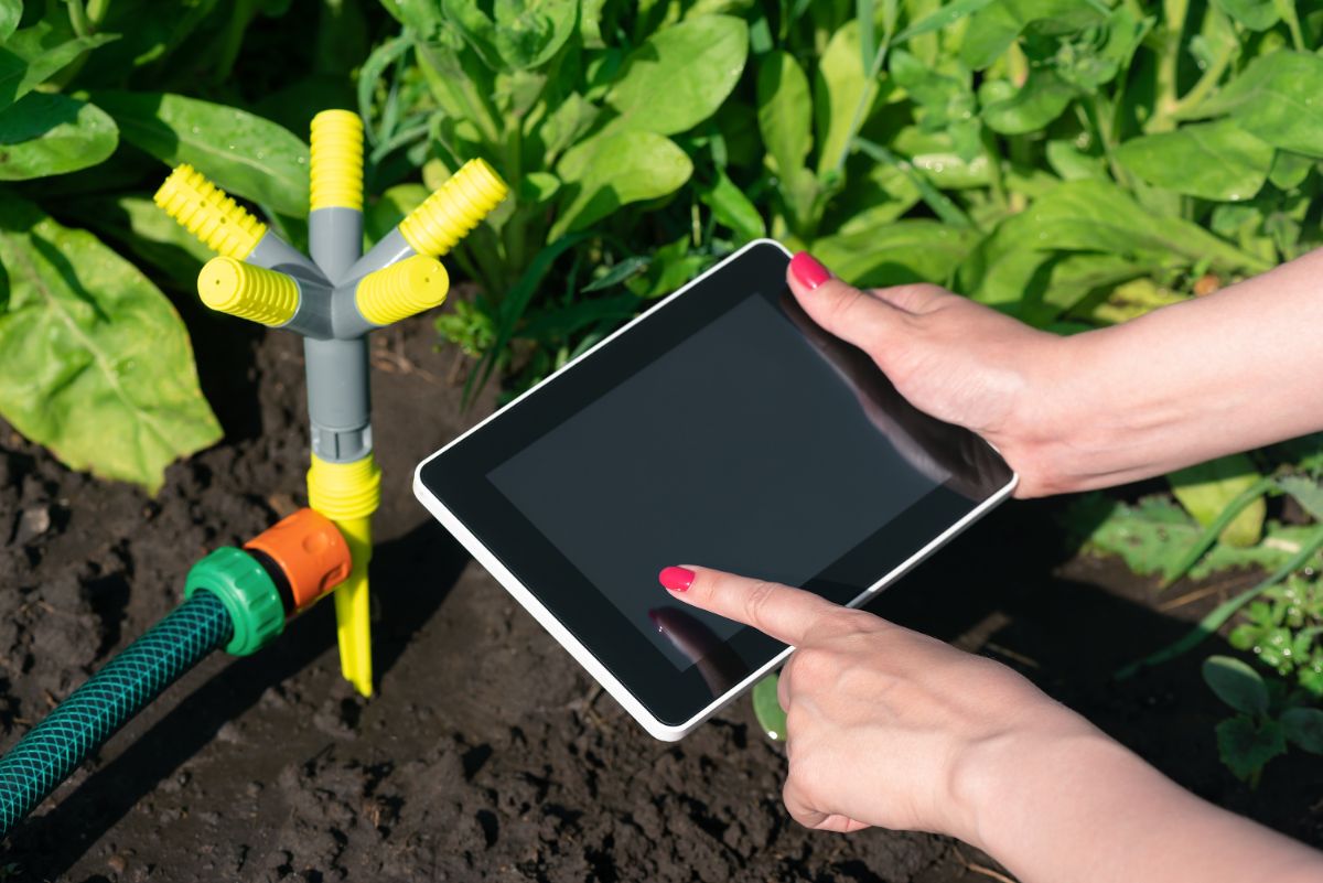 A woman's hand holding a tablet to control a smart sprinkler system