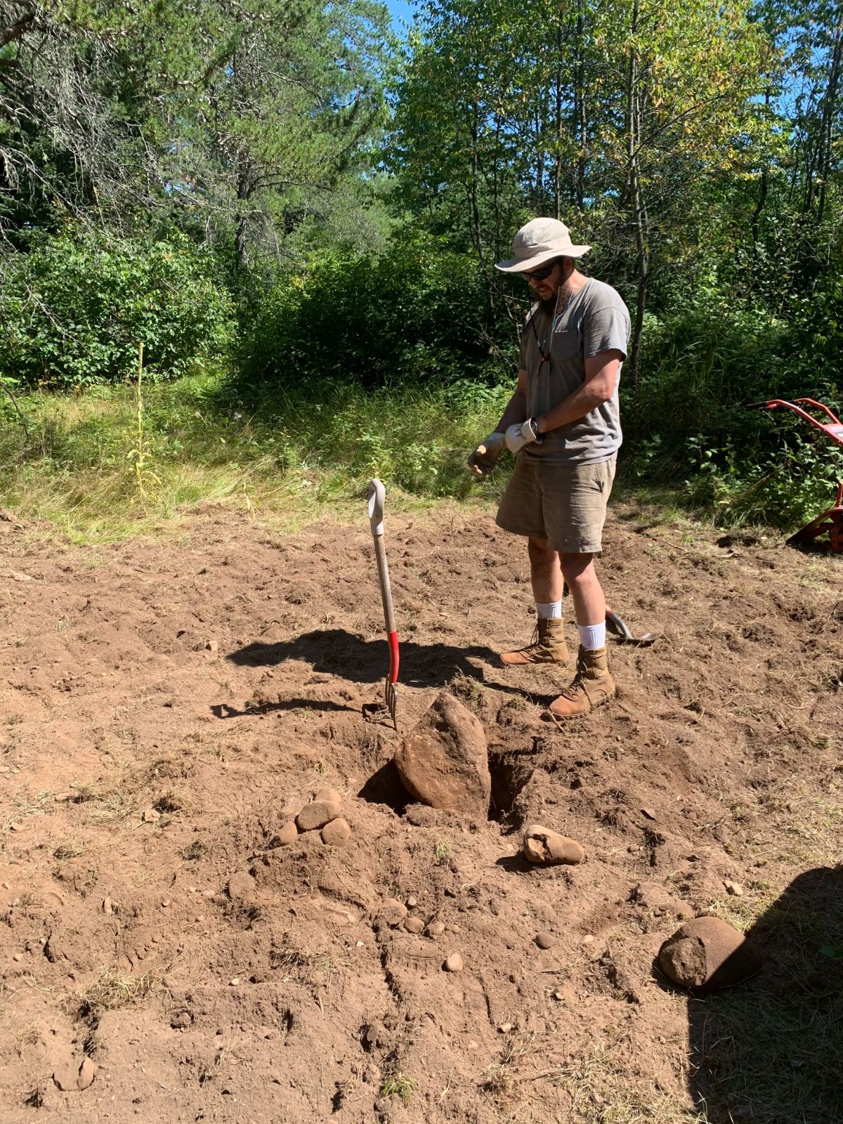 Man standing over a large rock in newly-tilled soil