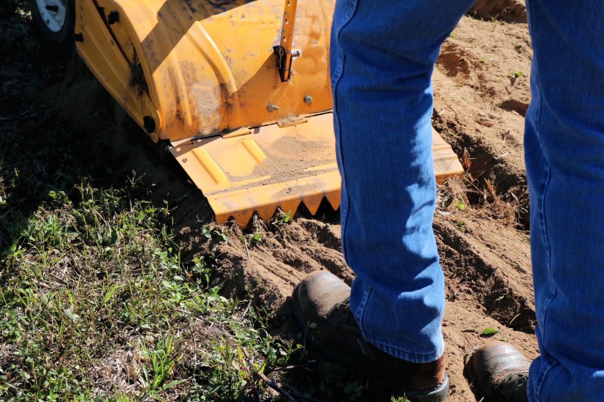 gardener walking behind a rototiller tilling a garden bed