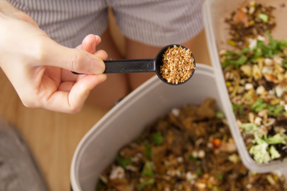 Person adding a spoonful of inoculated bran to Bokashi compost