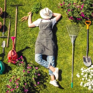 Girl lying on a green grass with gardening tools around.