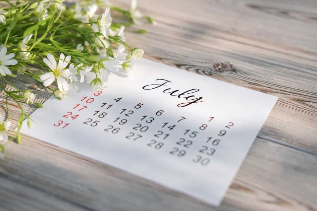 July calendar page with flowers on a wood table top