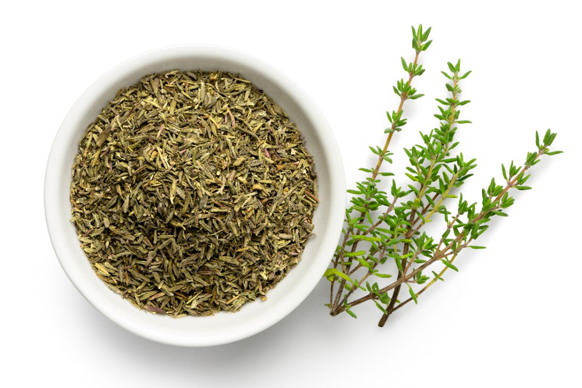 Sprigs of fresh thyme nest to a bowl of dried thyme leaves