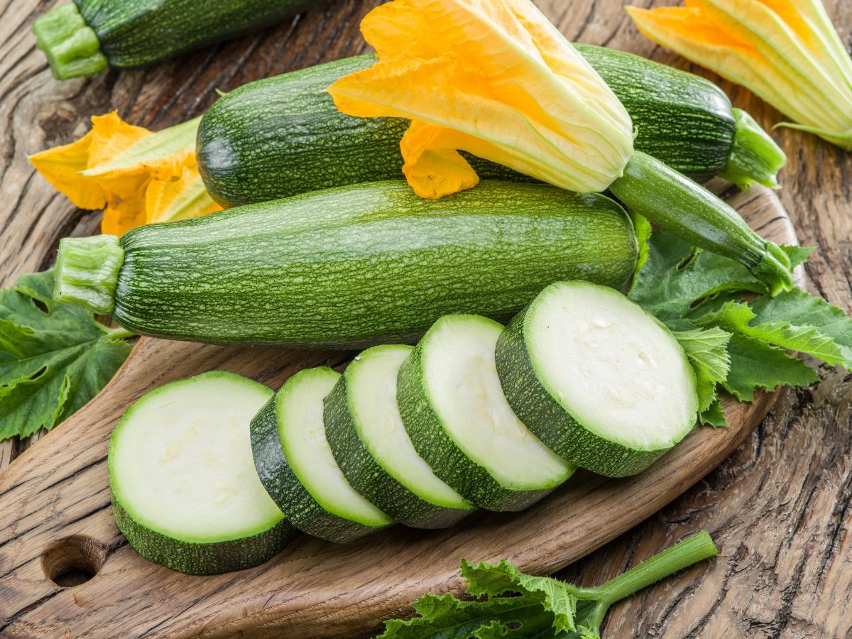 Sliced fresh zucchini on a board with zucchini blossoms