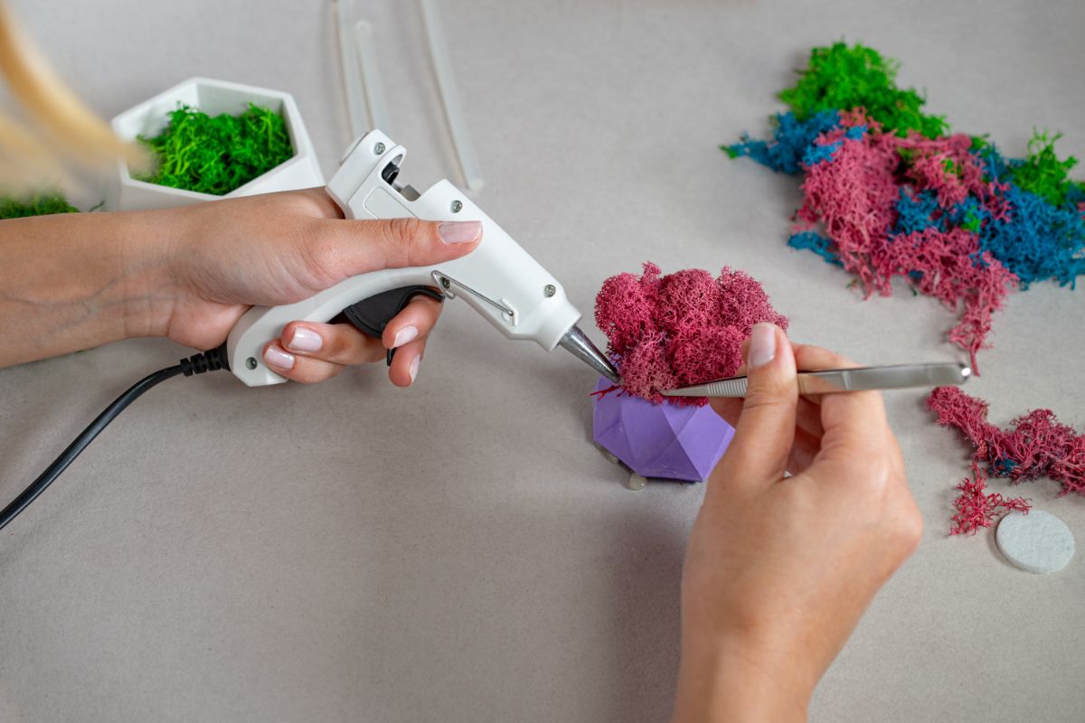 A crafter using a glue gun and craft supplies to create a pink bush for a fairy garden