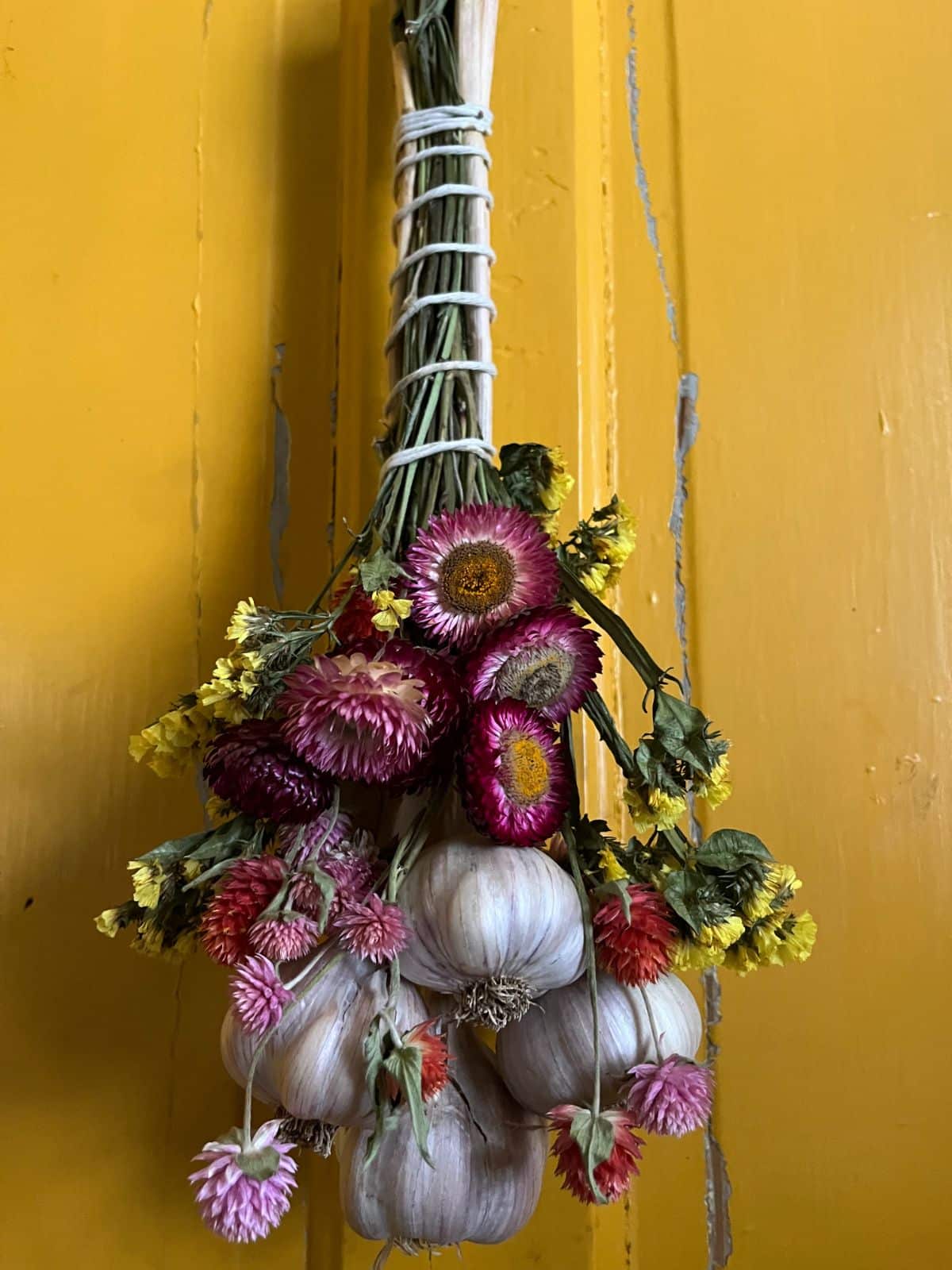 A bundle made of hardneck garlic and dry flowers hanging on a kitchen door