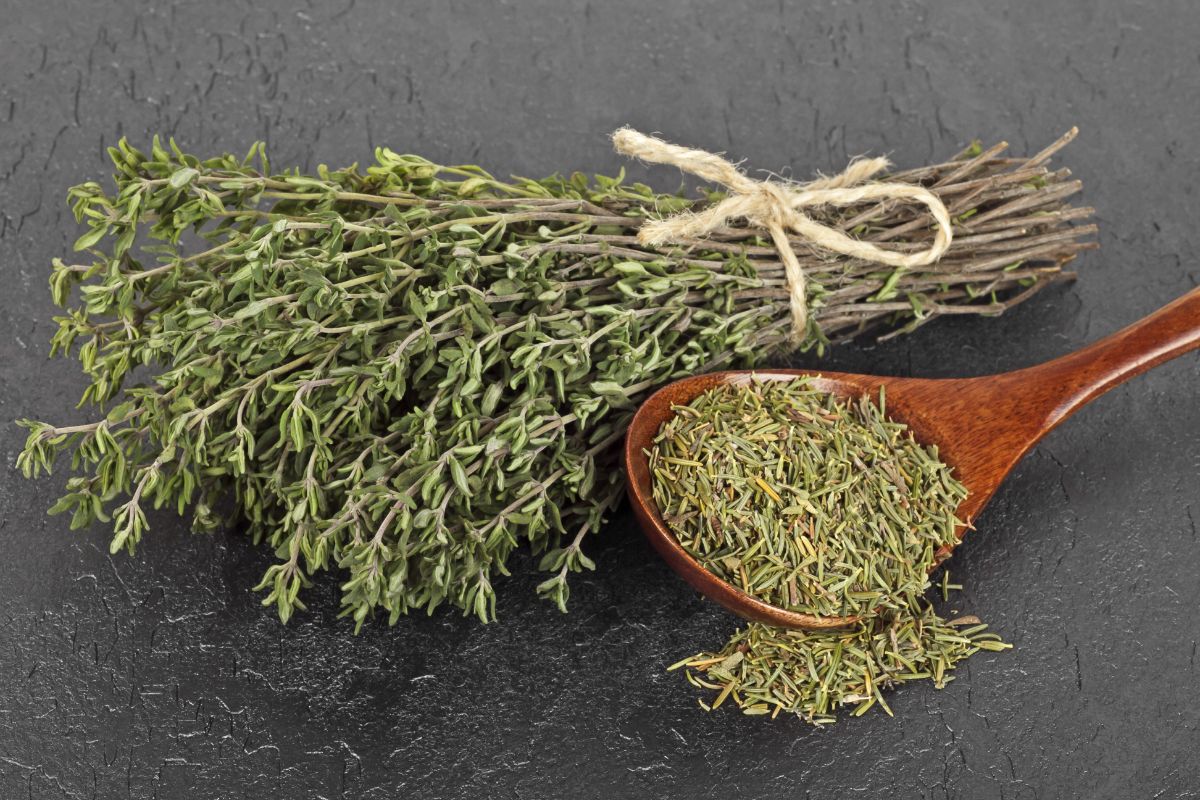 A bundle of dried thyme lying next to a bowl of dried thyme leaves
