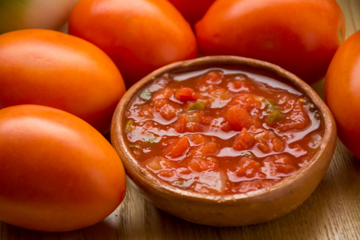 A bowl of homemade canned salsa sits next to ripe tomatoes