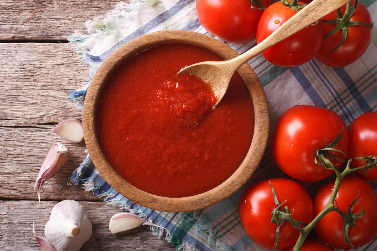 Clusters of ripe tomatoes sit next to dish of homemade tomato sauce.