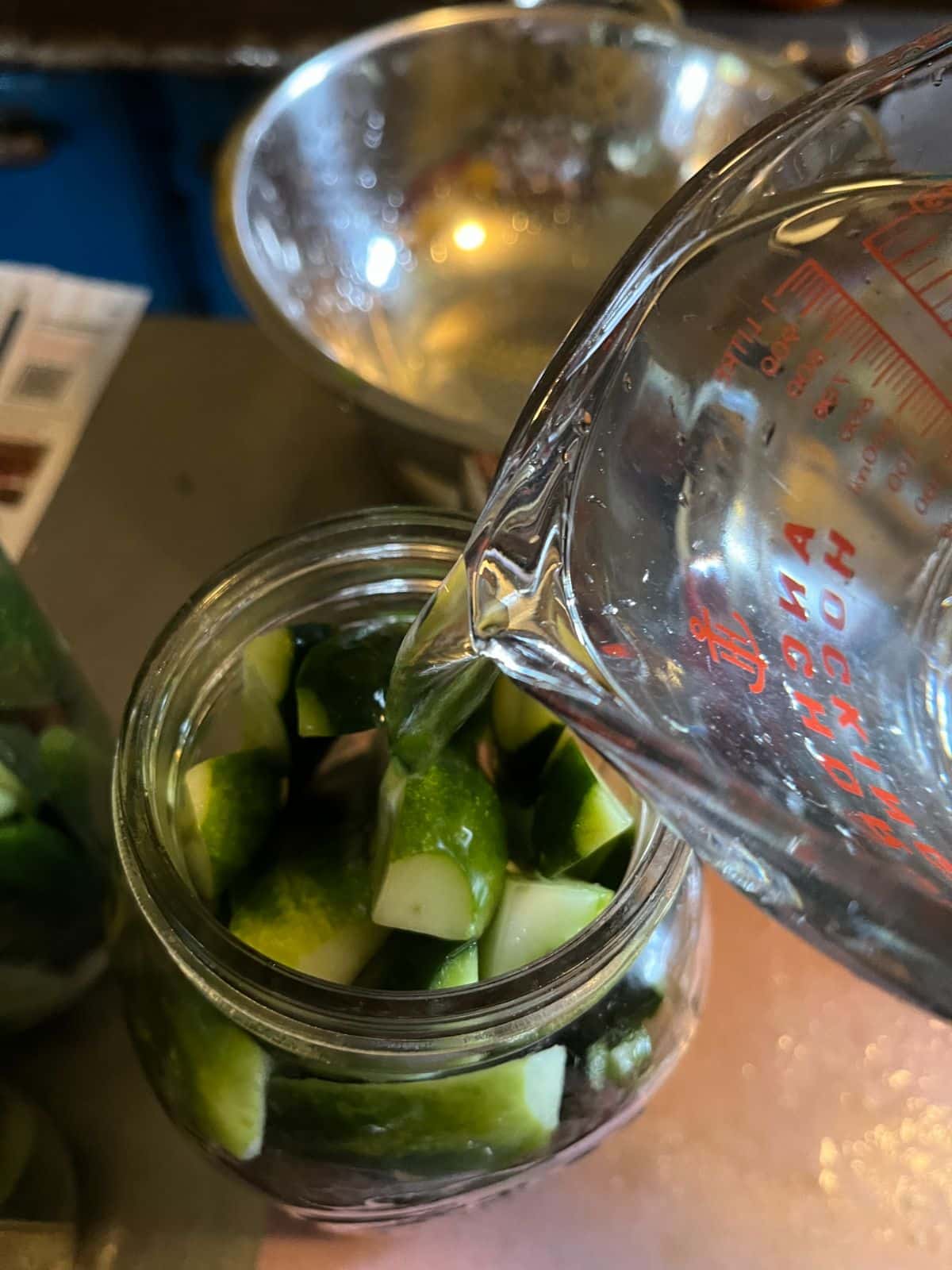 Pouring brine into a jar of cucumbers for pickling