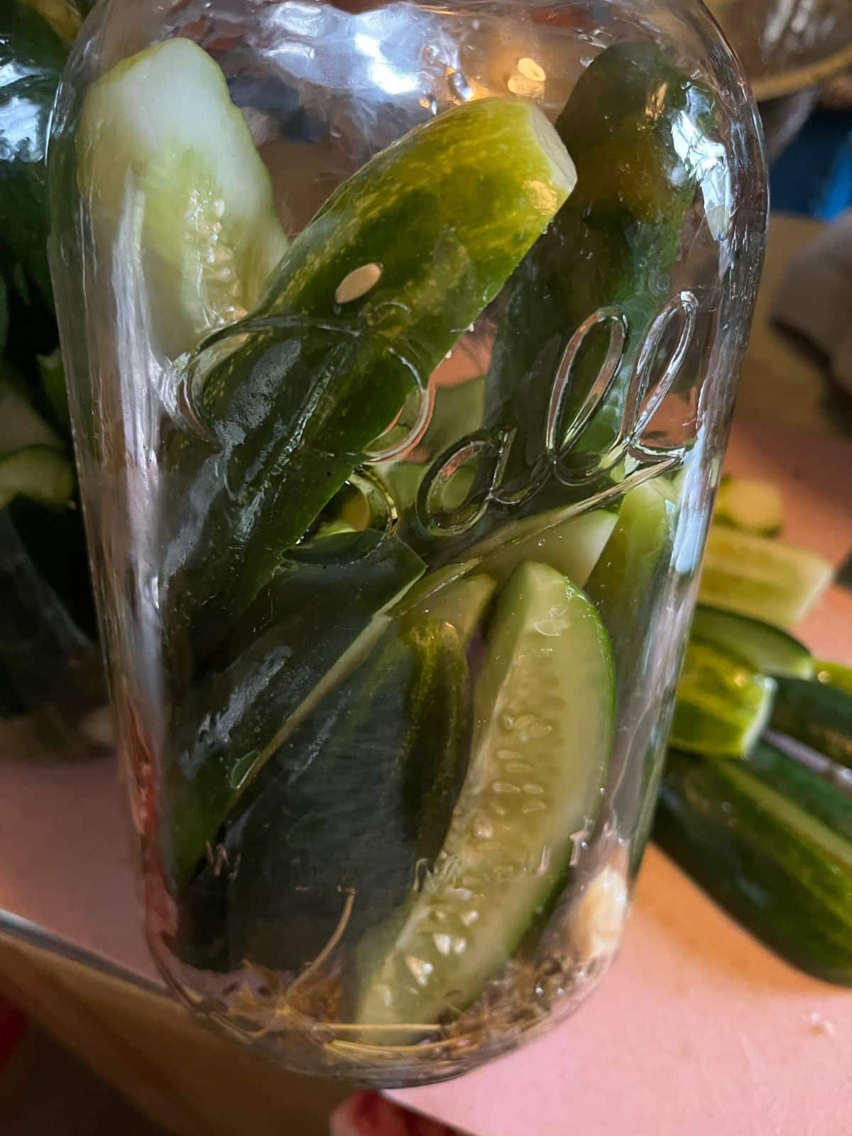 Cut cucumbers next to a jar of fresh pickles