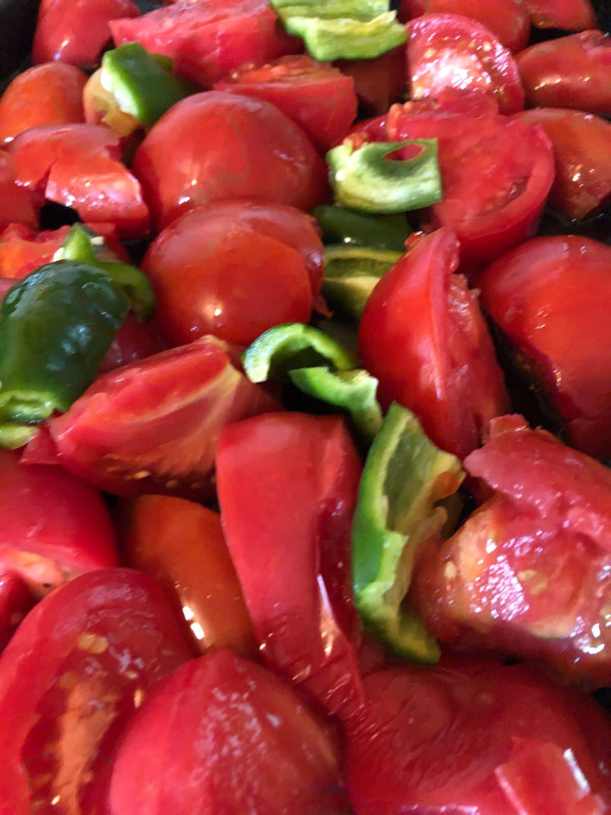 Quartered tomatoes spread out on a baking sheet with vegetables