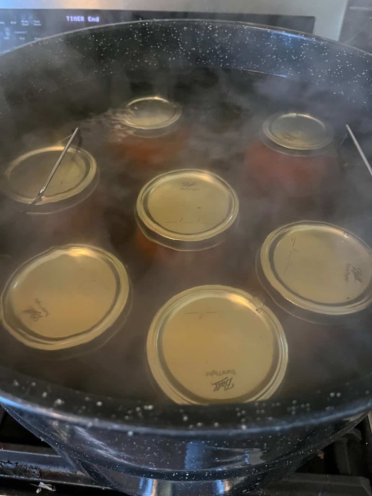 Jars of roasted tomato sauce being canned in a boiling water bath canner