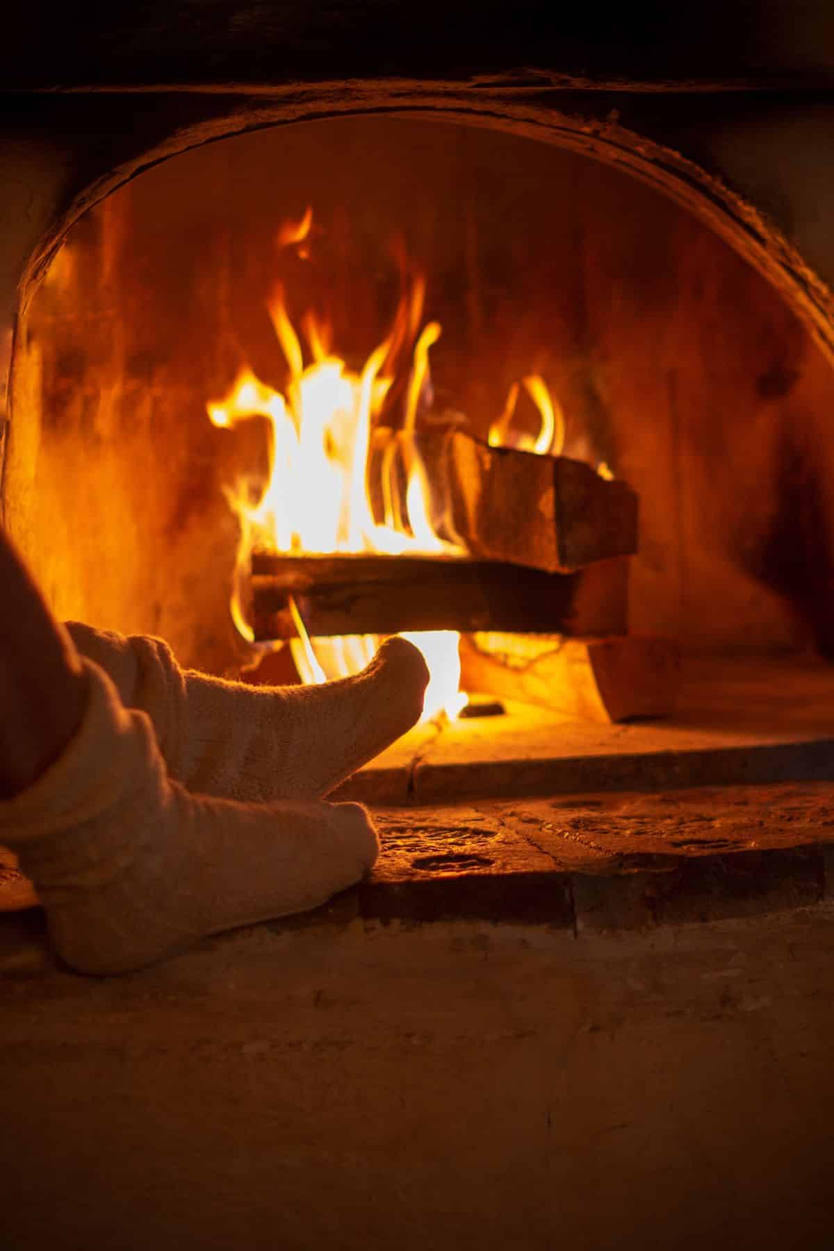 A woman’s feet warming by a fire in a fireplace.