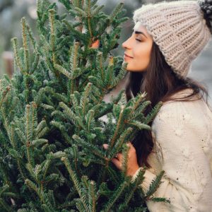 A young woman with a winter hat holding and sniffing a christmas tree.