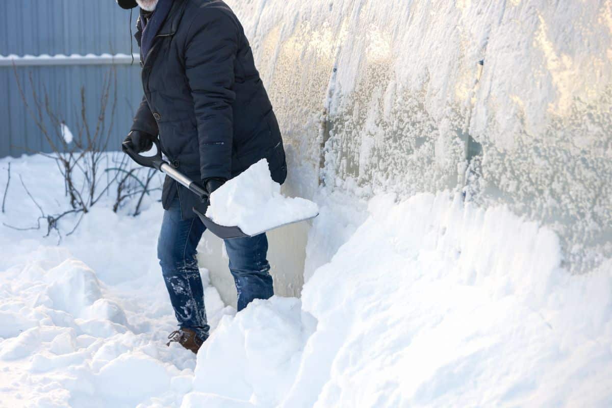 A man shovels snow outside a greenhouse.