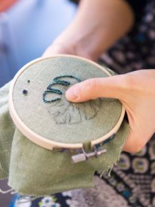 Hands of girl/woman/female sewing small embroidery pattern in a tiny wooden frame.