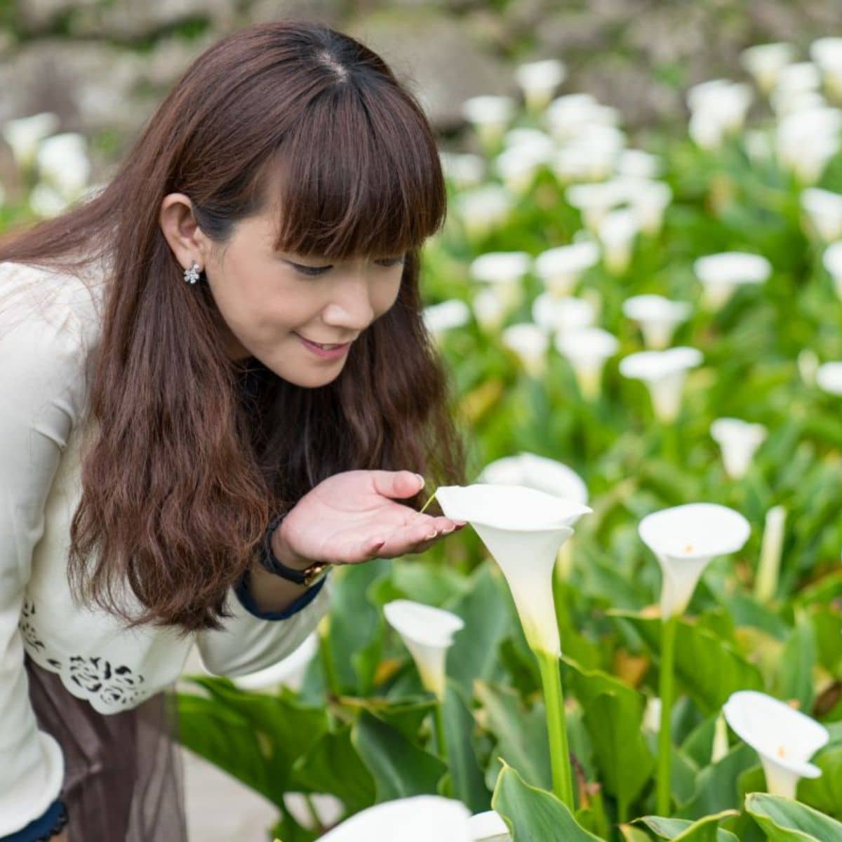 A young woman touching a white calla lily in a garden.