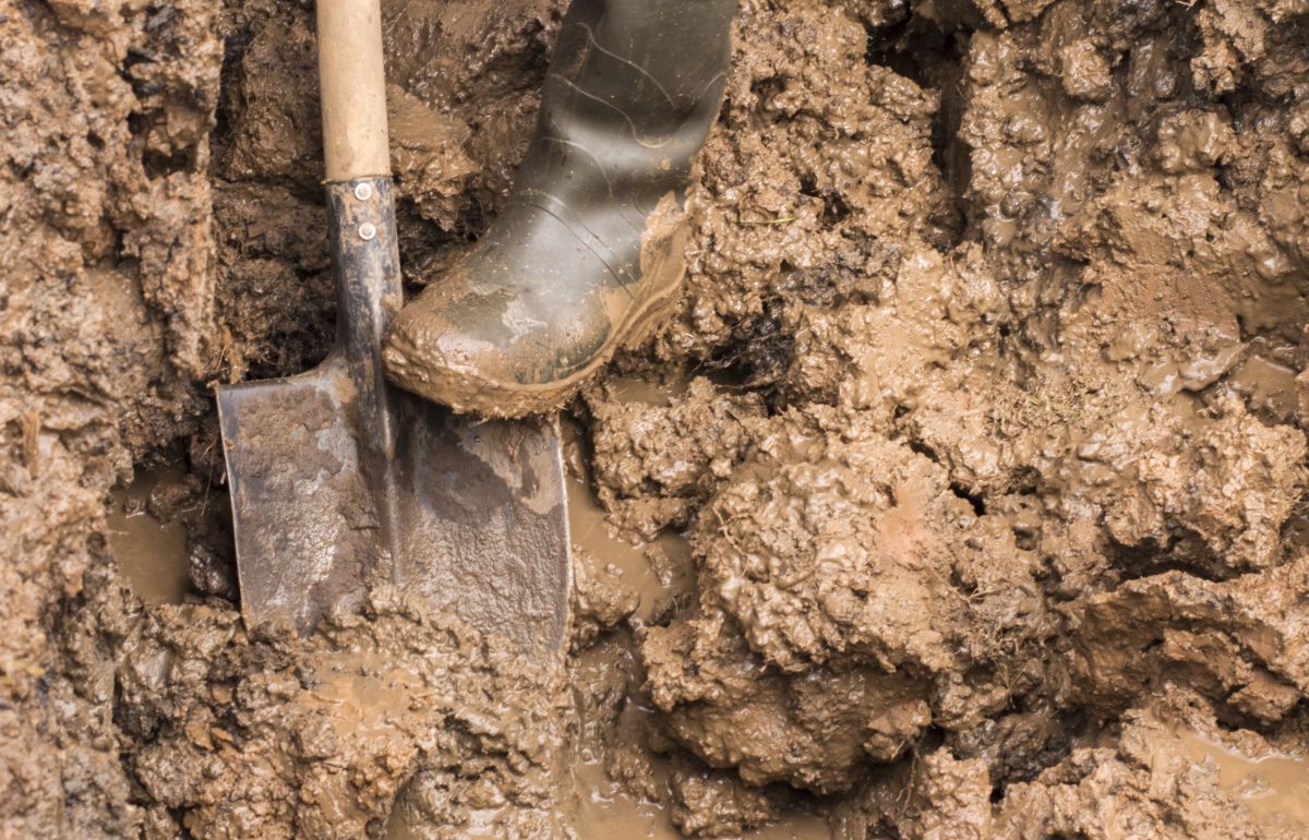 A shovel in muddy, wet clay soil