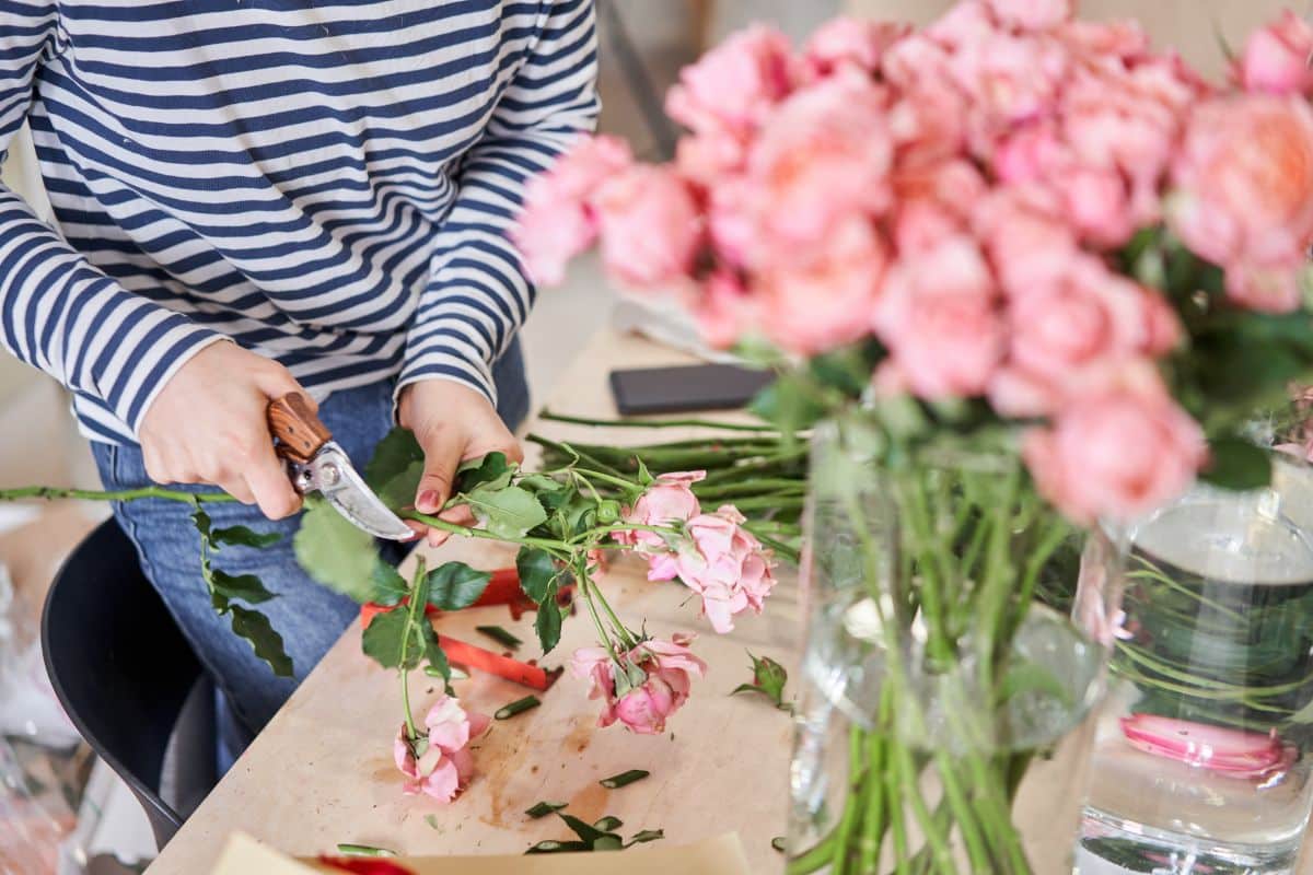 A woman trims lower leaves on a cut flower