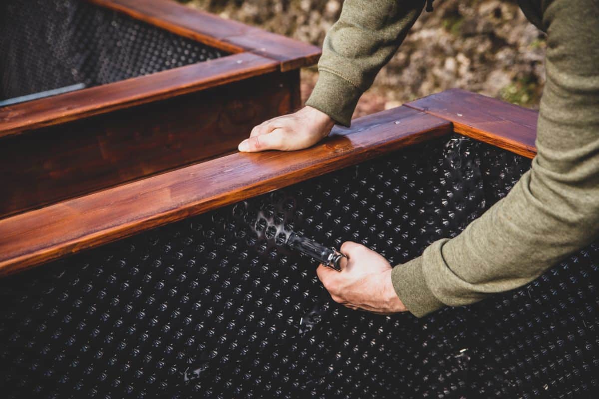 A man adds a liner to a raised bed garden bed