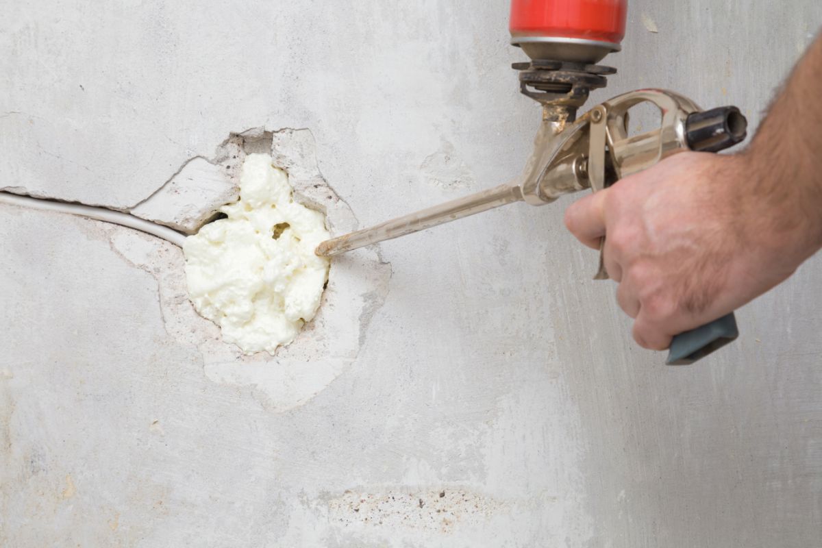 A homeowner fills a gap with spray foam to seal it off
