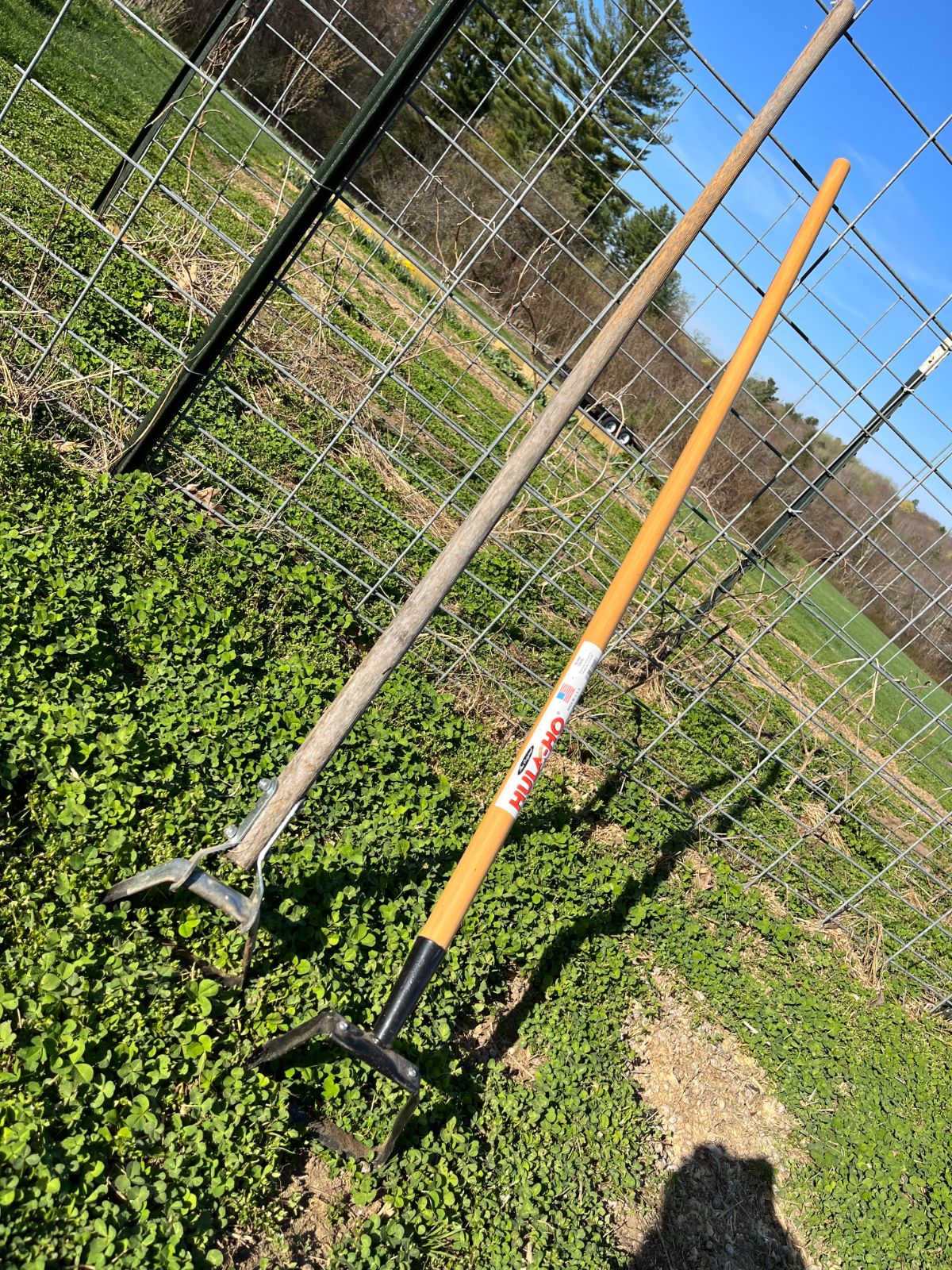 A hula hoe is leaned up against garden fencing
