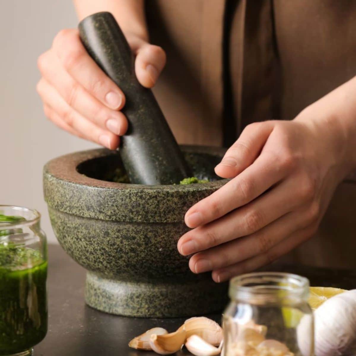 Woman making pesto sauce with mortar and pestle on a table in the kitchen