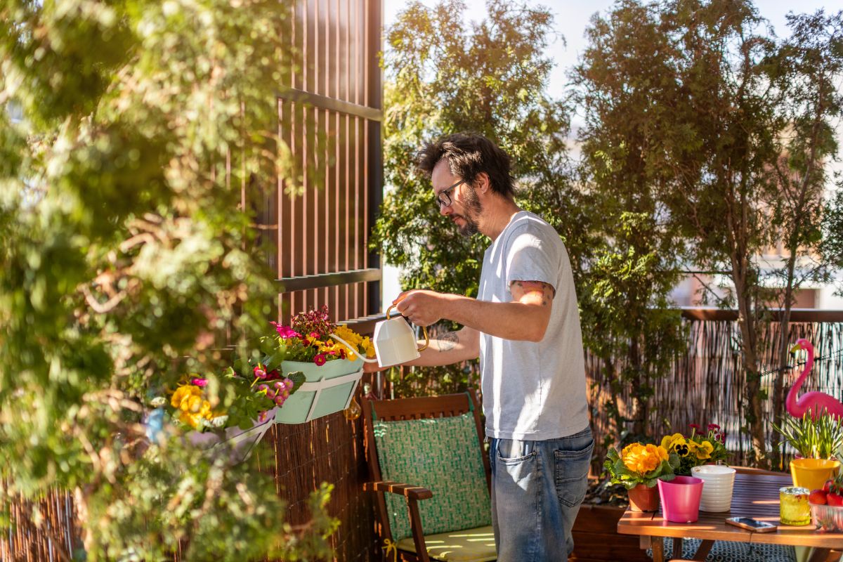 A man waters a planter box in a balcony garden