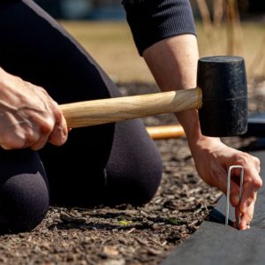 A gardener anchors a black sheeting with garden staples.