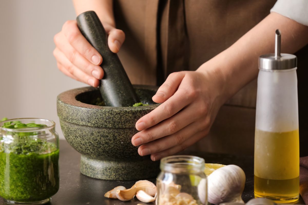 A person making pesto in a mortar and pestle