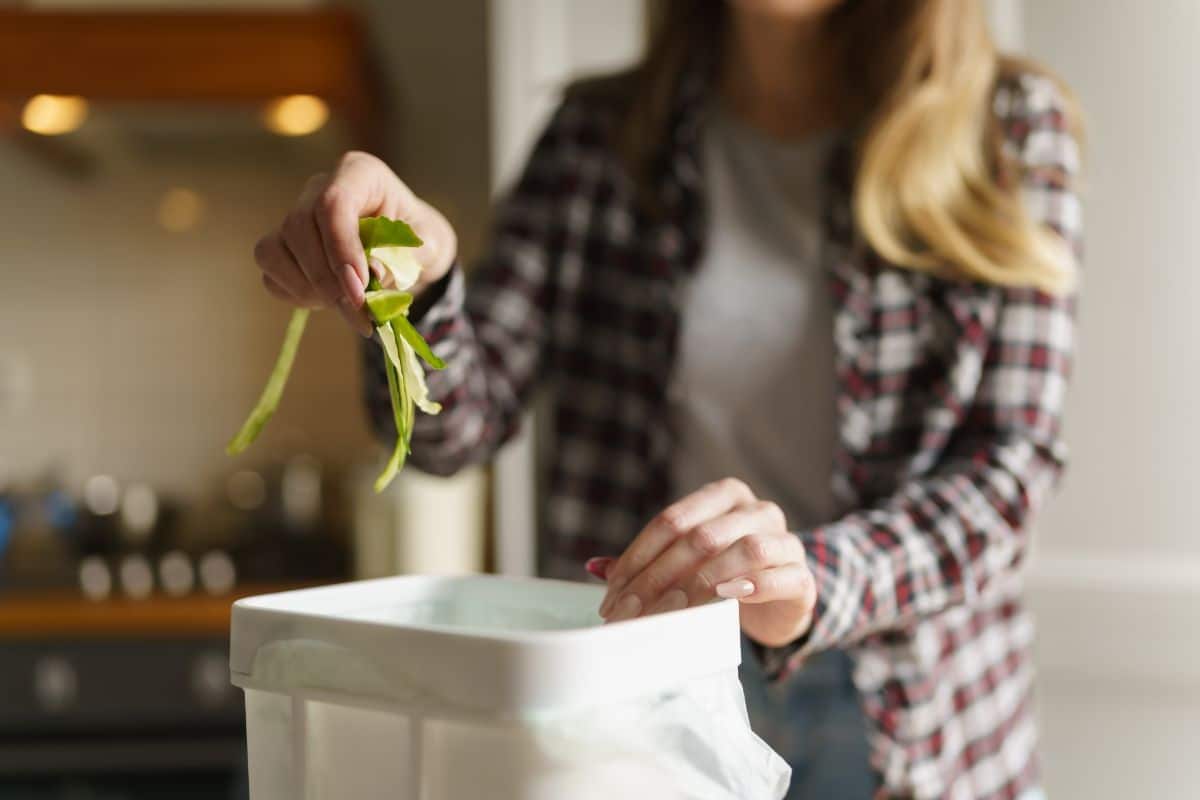 A woman adds cucumber peels to a compost bin