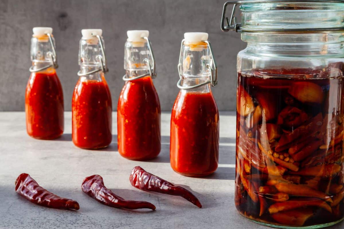 A jar of feremented peppers next to bottle of homemade hot sauce