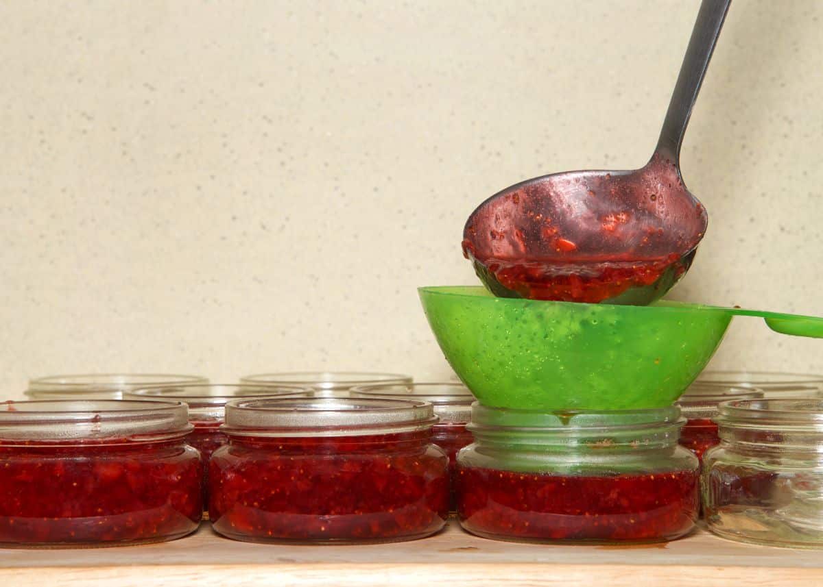 Fruit jam being ladled into clean jars for canning