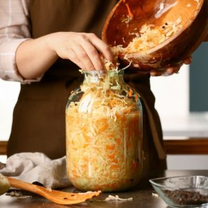 A woman puts tasty sauerkraut into a glass jar on the table in the kitchen.