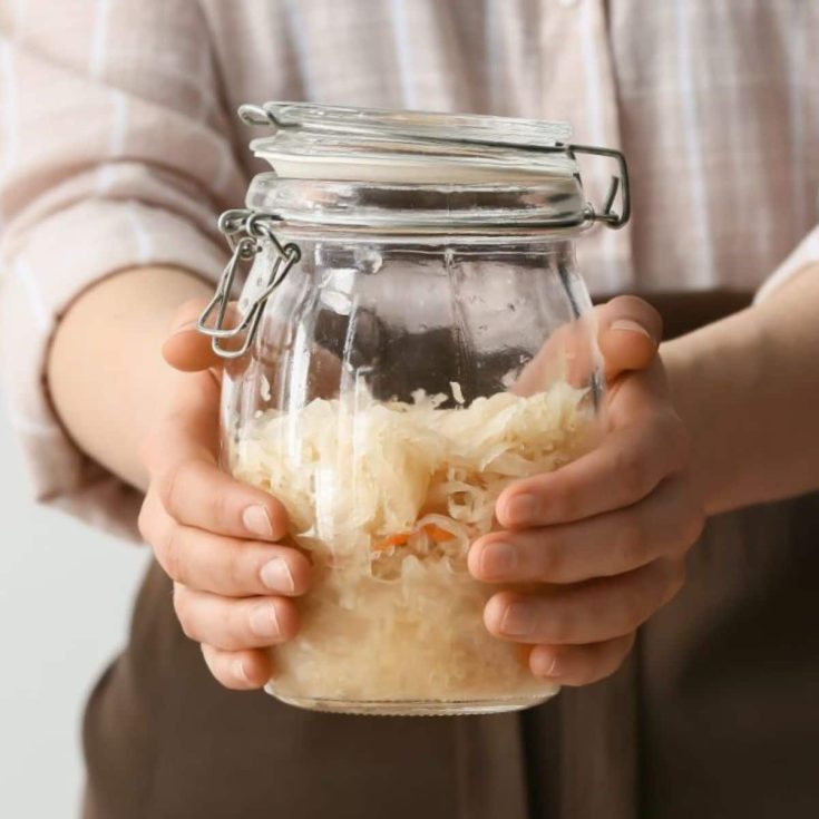 A woman holds a glass jar of tasty sauerkraut.