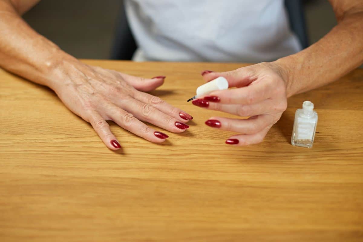 A woman paints on dark nail polish and nail hardener