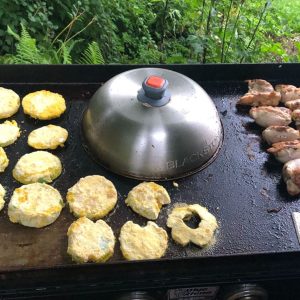 A flat top grill with veggies and meat.