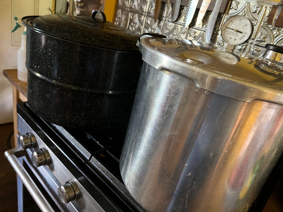 A water bath canner (black) and a pressure canner (silver) on a stove