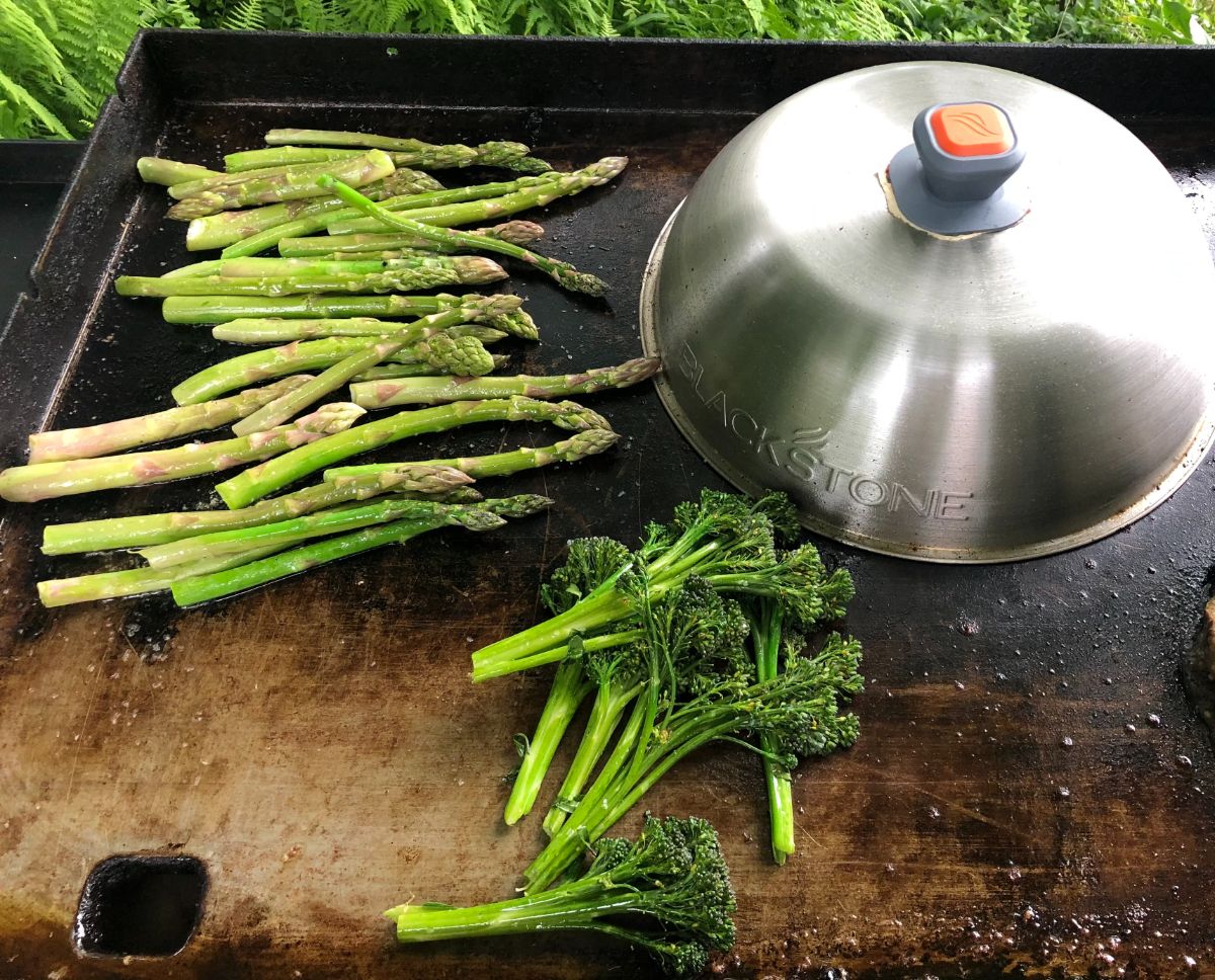 Broccoli spears and asparagus cooking on a flat grill