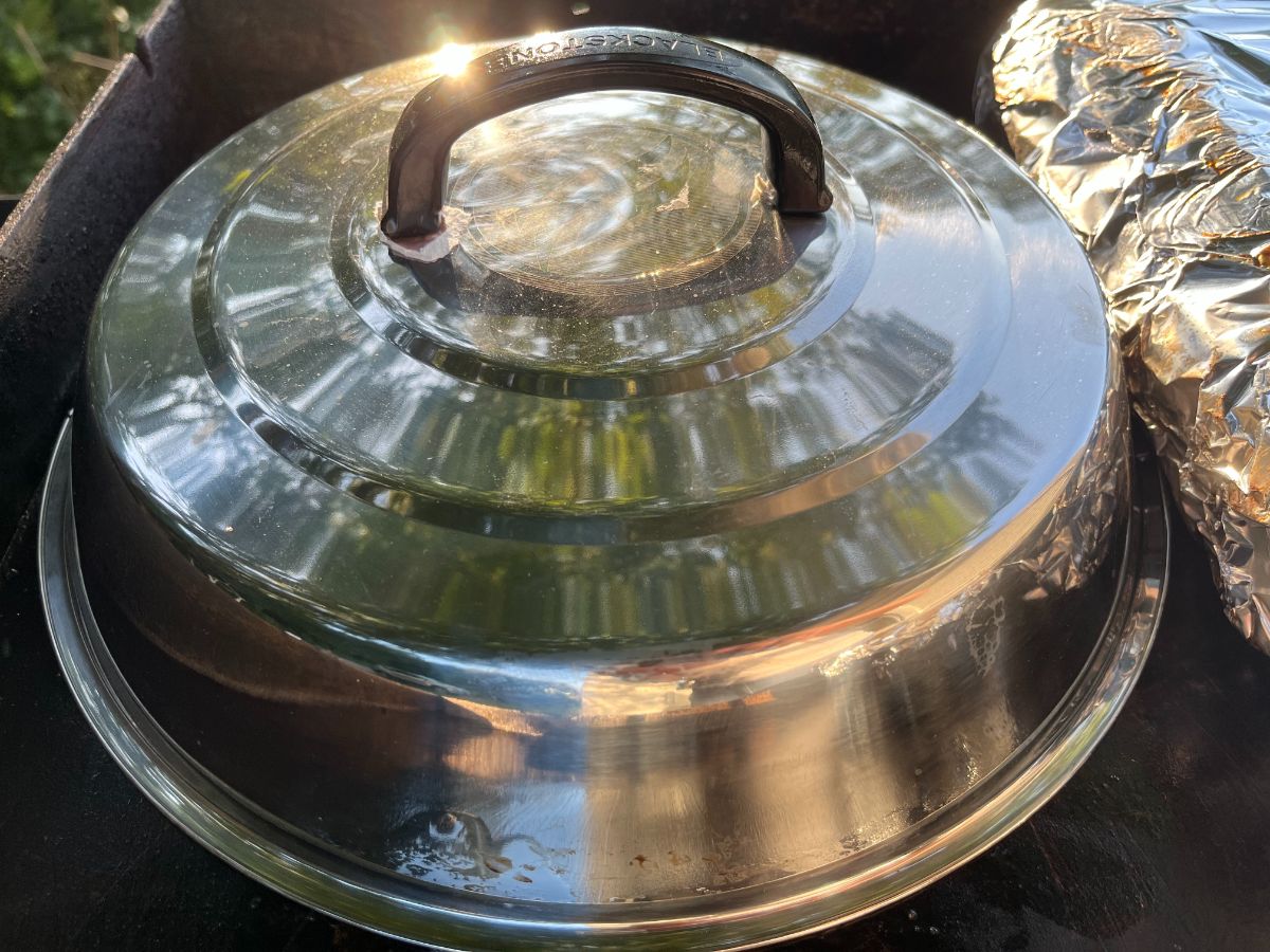 Vegetables cooking under a basting cover on a flat top grill