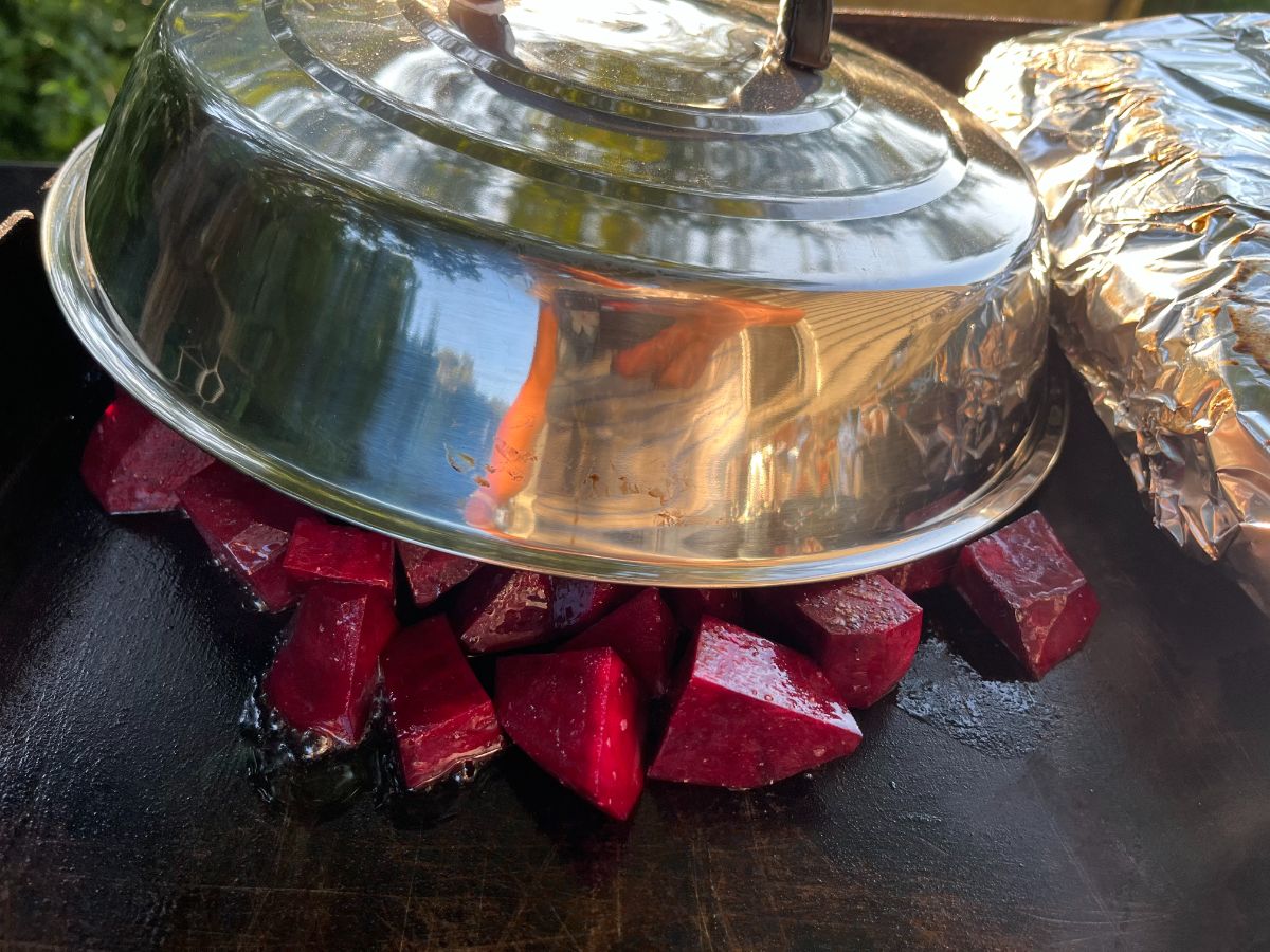 Grilled beets under a basting cover on a flat grill