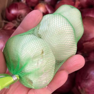 A hand holds a package of store-bought garlic.