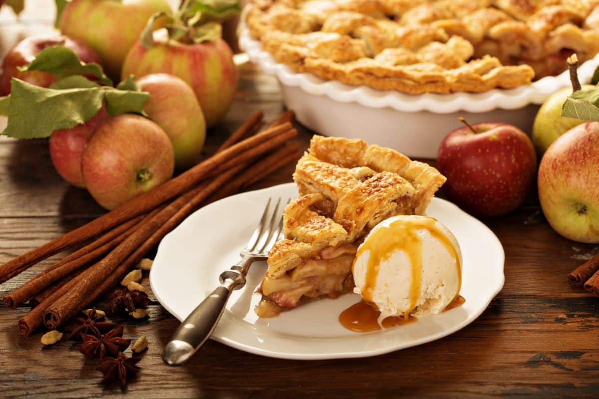 Apples surrounding a pieces of apple pie on a table setting