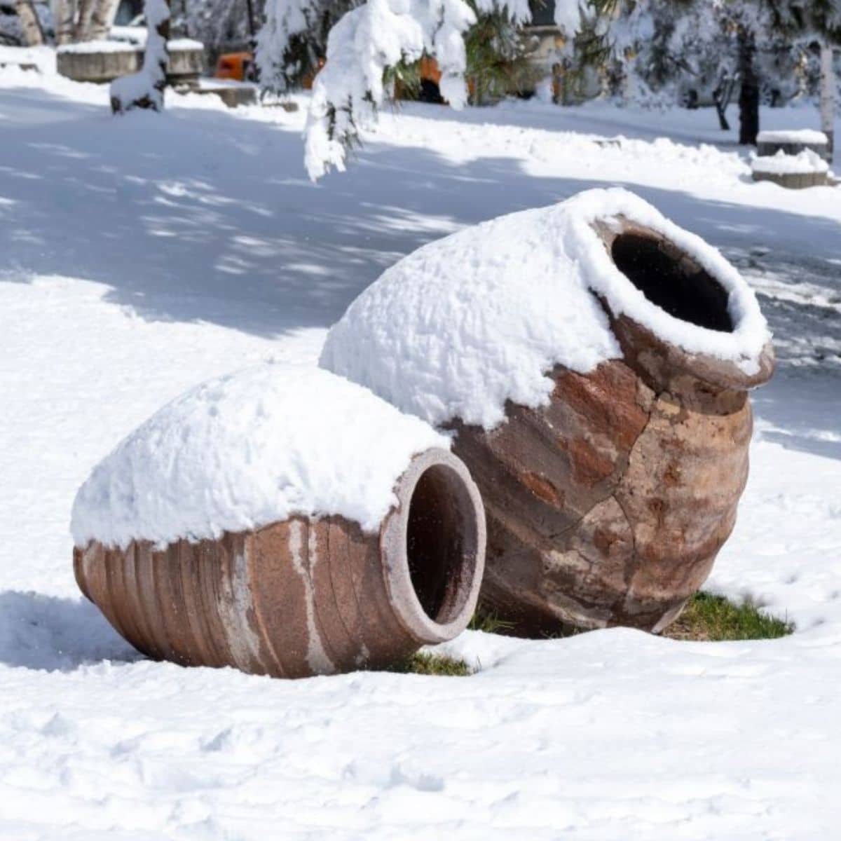 Two tilted large flower pots in the garden covered in snow.