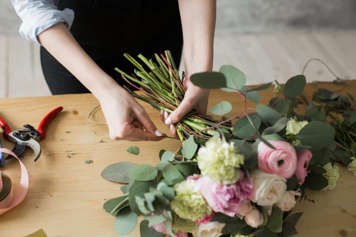 A florist making a bouquet with eucalyptus and ranunculuses